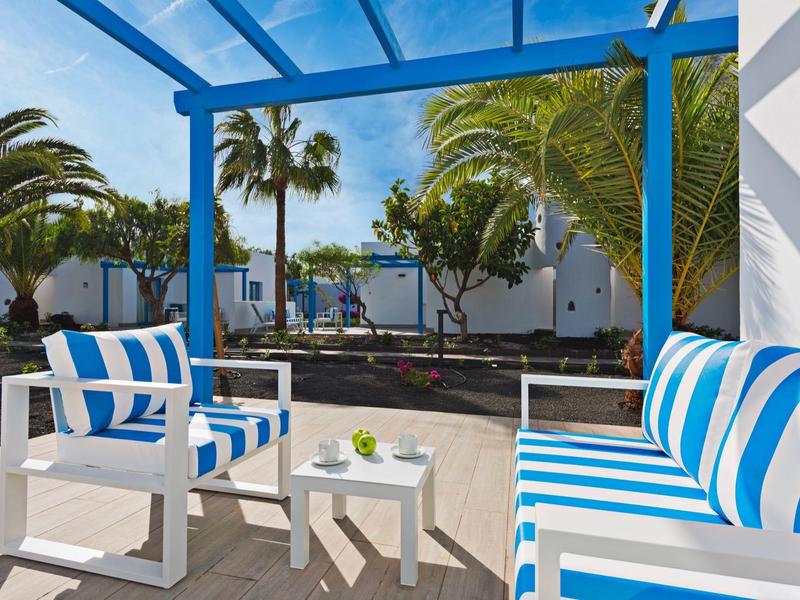 Terraza con muebles de rayas azul y blanco y vista a palmeras y edificios blancos.
