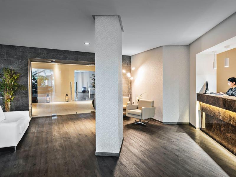 Área moderna del vestíbulo del hotel con recepción, asientos y suelo de madera oscura.