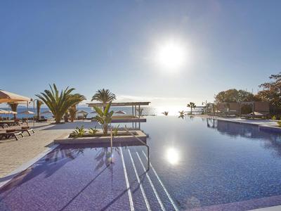 Großer Pool mit klarem Wasser, Liegestühlen und Palmen, Sonnenlicht und blauem Himmel.