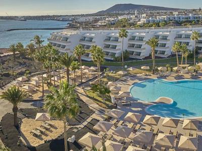 Große Hotelanlage mit mehreren Pools, vielen Liegen, Palmen und Meer im Hintergrund bei Sonnenuntergang.