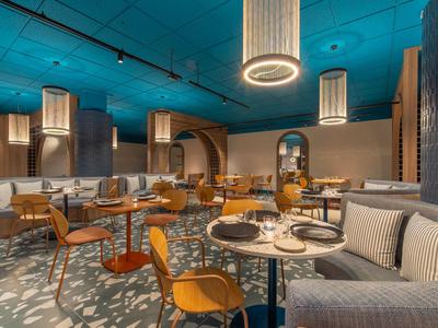 Modernes Restaurantinterieur mit rundem, blau beleuchtetem Deckenakzent und komfortablen Sitzbereichen.