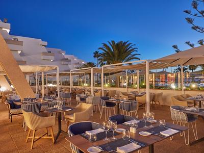 Außenrestaurant mit gedeckten Tischen und Stühlen unter blauer Abendhimmel.