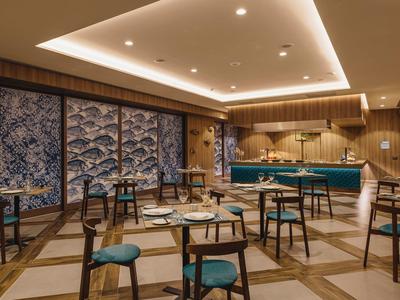 Moderner Gastraum mit Holzwänden, blau-grünen Stühlen und beleuchtetem Tresen in warmem Licht.