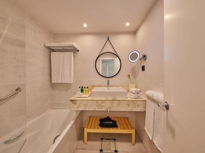 Helles Badezimmer mit Badewanne, rundem Spiegel, Waschbecken, Wandbeleuchtung und Handtüchern.