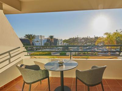 Balkon mit zwei grauen Stühlen, kleinem runden Tisch, rote Fliesen und sonniger Ausblick.