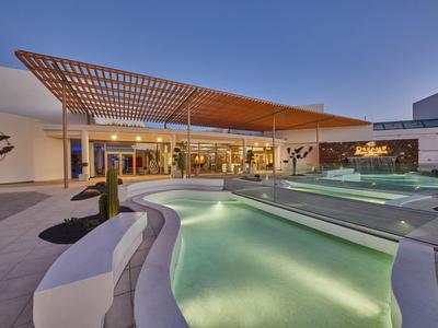 Moderner Außenbereich mit beleuchtetem Pool, Lounge-Möbeln und Holzpergola bei Dämmerung.