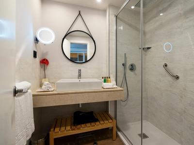 Modernes Badezimmer mit rundem Spiegel, hellem Waschbecken, Holzgitterregal und Glasdusche.