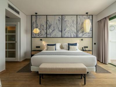 Modernes Schlafzimmer mit großem Bett, Holzfußboden, Kunstwerken über dem Kopfteil und Balkonzugang.