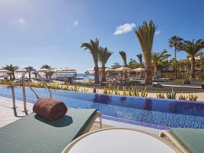 Poolbereich mit Sonnenliegen, Handtüchern und Palmen in einem sonnigen Resort.