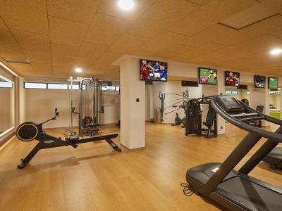 Moderner Fitnessraum mit verschiedenen Trainingsgeräten und Holzboden in einem Hotel.