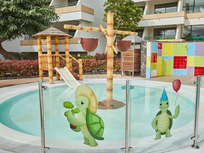 Kleines rundes Planschbecken mit bunten Dinosaurierfiguren und Wasserspielen hinter Glaszaun.