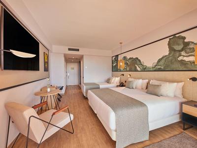 Helles Hotelzimmer mit großem Doppelbett, Holzfußboden, Wandbild und gemütlicher Sitzcke.