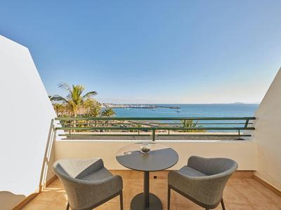Balkon mit zwei grauen Stühlen und kleinem Tisch mit Meerblick bei klarem Himmel.