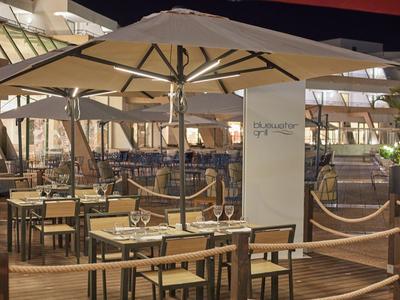 Freiluftrestaurant mit Holztischen, Stühlen, großen Sonnenschirmen und gedämpfter Beleuchtung bei Nacht.