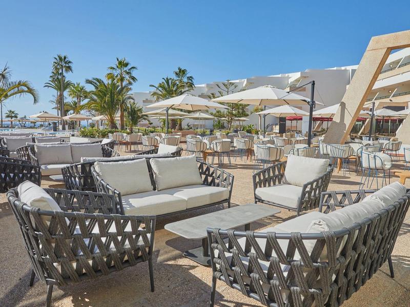 Große Terrasse mit bequemen Sitzgruppen aus grauem geflochtenem Material und weißen Kissen.