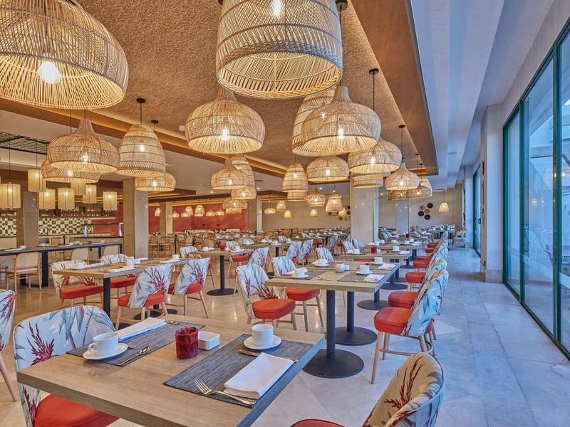 Großes modernes Restaurant mit Holztischen, roten Stühlen und vielen Rattanlampen an der Decke.