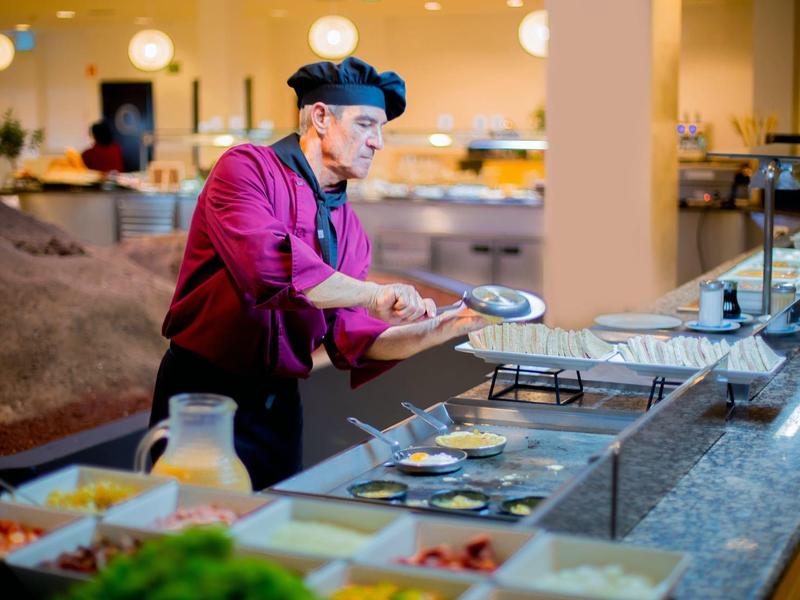 Mann mit Kochmütze nimmt Essen vom Buffet in einem hellen Speisesaal.