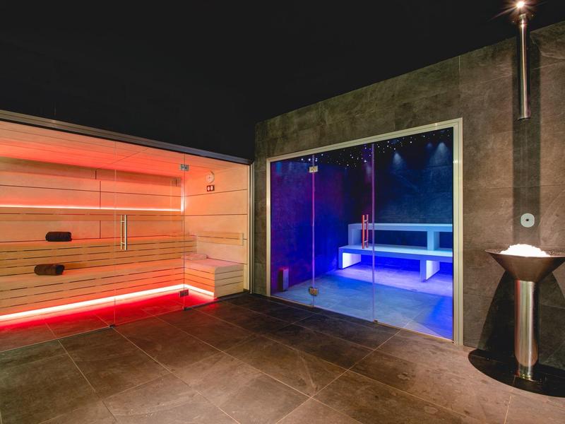 Moderne Sauna mit roten LED-Lichtern und angrenzendem beheiztem Pool mit blauer Beleuchtung.