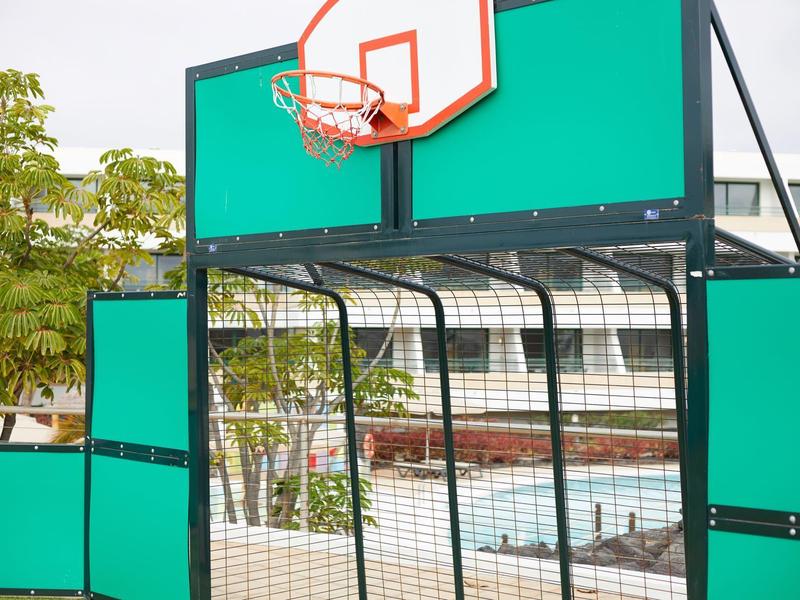 Kleines Basketballfeld mit grünem Rückenbrett und rotem Korb im Freien bei Tageslicht.
