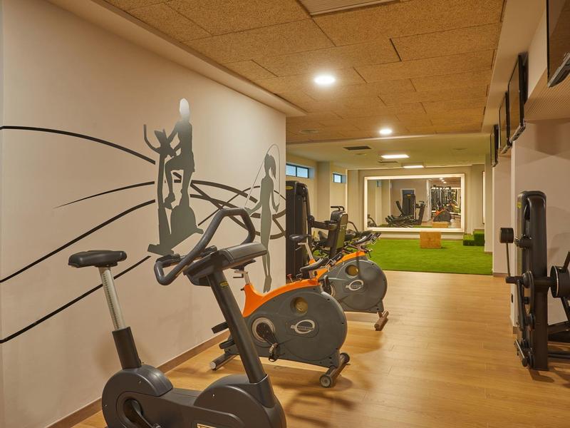 Innenraum eines Fitnessraums mit mehreren Ergometern, Holzboden und hellen Deckenleuchten.