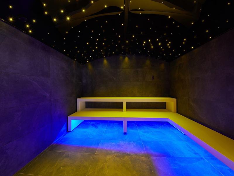 Raum mit L-förmiger Bank, blauer Bodenbeleuchtung und Sternenhimmel-Decke in dunkler Atmosphäre.