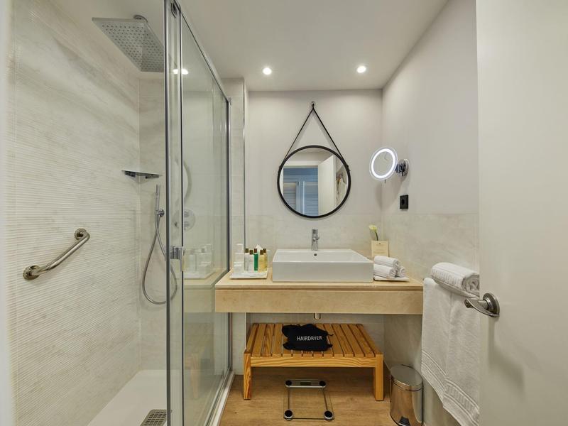 Kompaktes Badezimmer mit Glasdusche, Holzwaschtisch, rundem Spiegel und modernem Waschtischambiente.