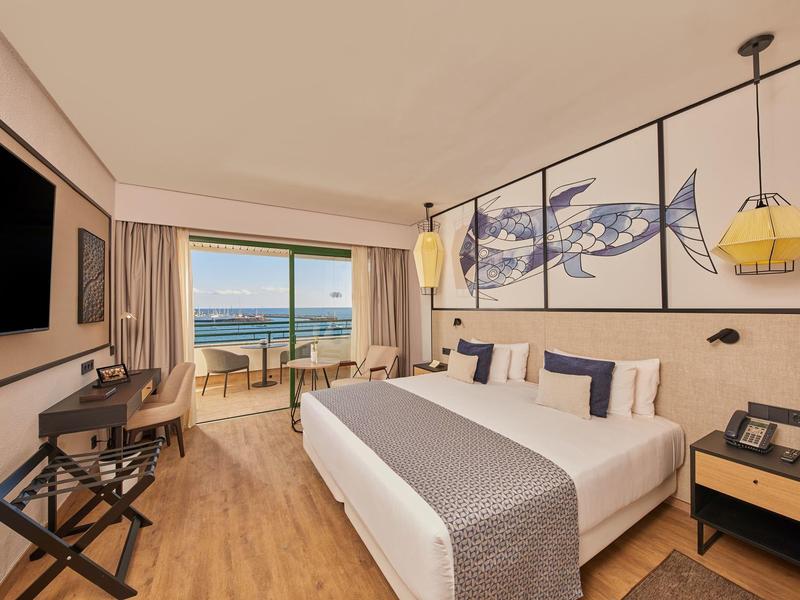 Modernes Hotelzimmer mit Doppelbett, Meerblick, Holzboden und maritimer Wanddekoration.