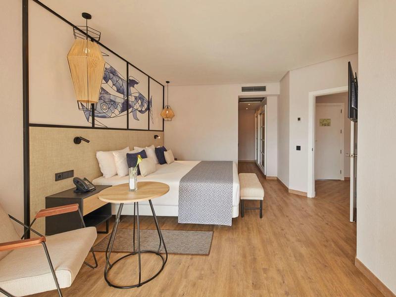 Modern eingerichtetes Hotelzimmer mit Doppelbett, Holzboden, runden Tischen und Wandbildern.