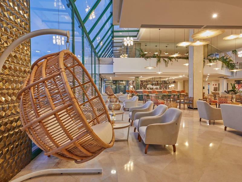 Moderner Innenraum mit hängendem Korbsessel, grauen Sesseln und hellem Marmorboden.