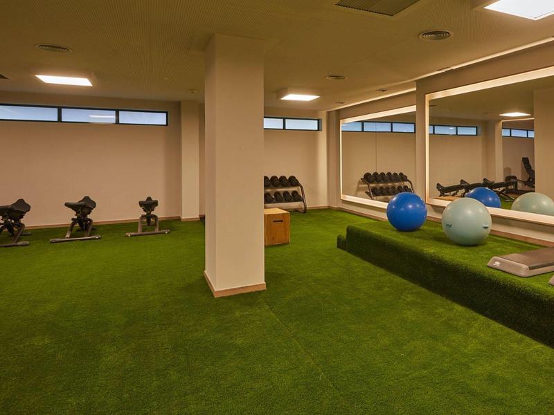 Innenraum eines gut beleuchteten Fitnessraums mit grünen Teppichboden und Trainingsgeräten.