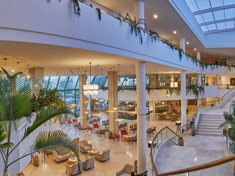 Großes, modernes Einkaufszentrum mit heller Atmosphäre, Glasdach und Pflanzen im Innenraum.