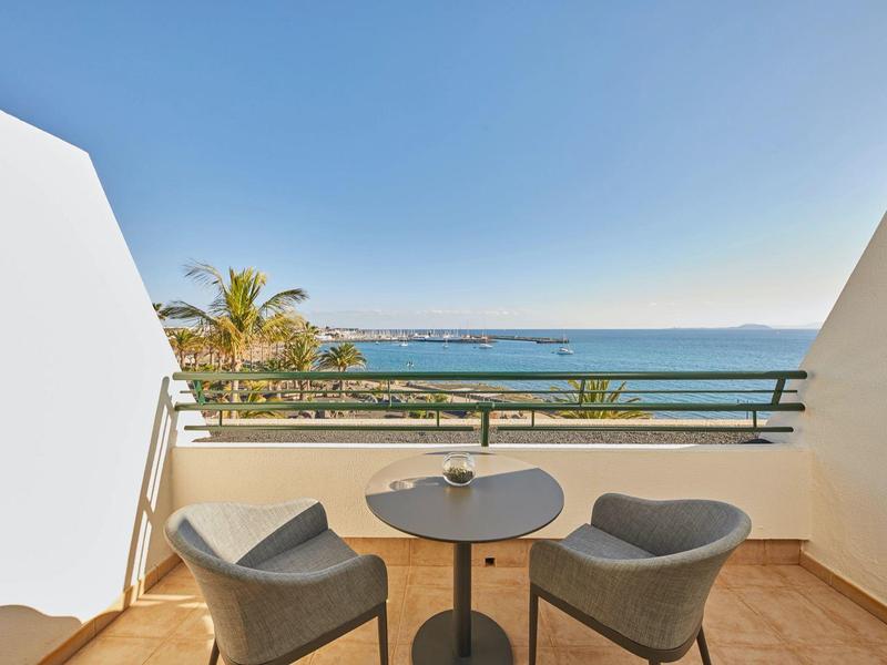 Balkon mit zwei grauen Stühlen und kleinem Tisch mit Meerblick bei klarem Himmel.