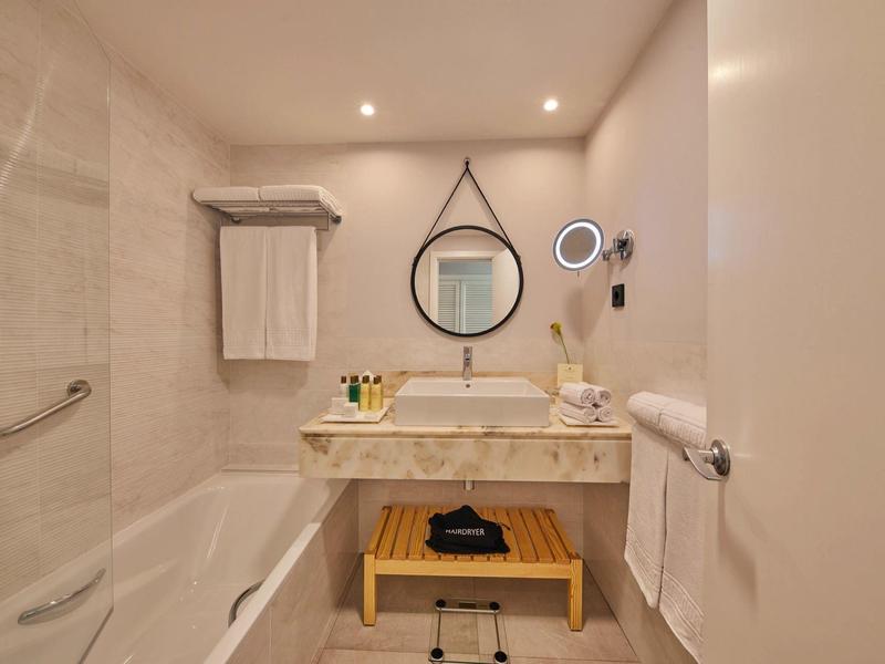 Helles, modernes Badezimmer mit Badewanne, rundem Spiegel und Holzregal unter dem Waschbecken.