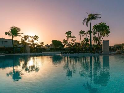 Ein ruhiger Hotelpool bei Sonnenuntergang mit Palmen im Hintergrund.
