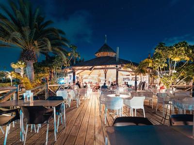 Abendlicher Außenbereich eines Hotels mit gedeckten Tischen und Palmen am Holzsteg.