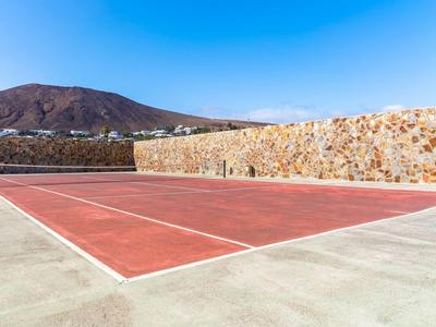 Ein leerer, roter Tennisplatz mit Bergen im Hintergrund unter klarem blauem Himmel.