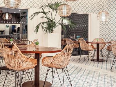 Moderner Hotel-Loungebereich mit Flechtstühlen, runden Holztischen und Pflanzen.