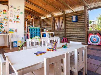 Kinderzimmer mit bunten Spielzeugen, weißen Tischen und Stühlen in einem hellen Raum mit Holzdecke.