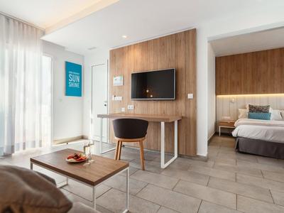 Modern eingerichtetes Hotelzimmer mit Balkon, Fernseher und angrenzendem Schlafzimmer.