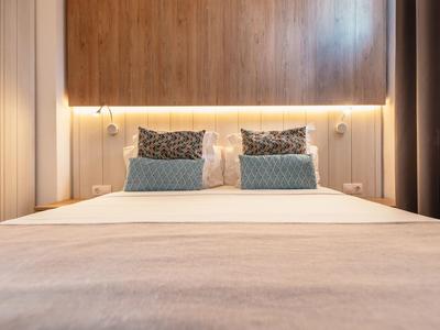 Modernes Hotelzimmer mit Holzwand, zwei Kissen und warmem Licht über dem Bett.
