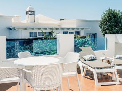 Moderne Terrasse mit weißem Mobiliar, Pool und klarer blauer Himmel im Hintergrund.