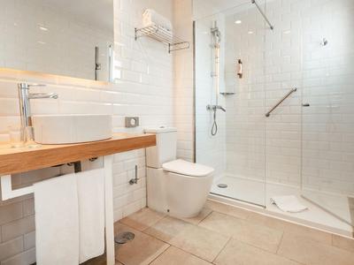Hell beleuchtetes Badezimmer mit Holzwaschtisch, Toilette und begehbarer Dusche mit Glaswand.