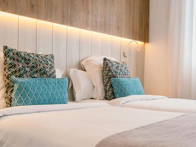Modernes Hotelzimmer mit bequemem Bett, gemusterten Kissen und warmem Licht hinter dem Kopfteil.