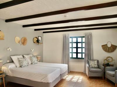 Helles Schlafzimmer mit zwei Einzelbetten, grauen Wänden, Holzbalken und Fenster mit Gardinen.