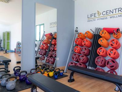 Fitnessstudio mit Hantelbänken, Gewichten und bunten Yogamatten an der Wand