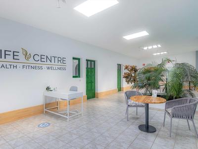 Heller, moderner Flur mit Pflanzen, Sitzbereich und grünen Türen im Gesundheitszentrum.