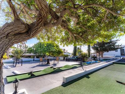 Außenbereich mit Minigolfanlage, umgeben von Bäumen und Sitzbereichen unter klarem Himmel.