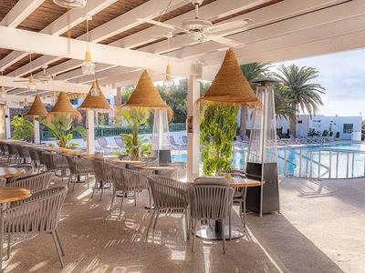 Offener Restaurantbereich mit Korbstühlen, weißen Tischen und großen Rattanlampen neben Pool.