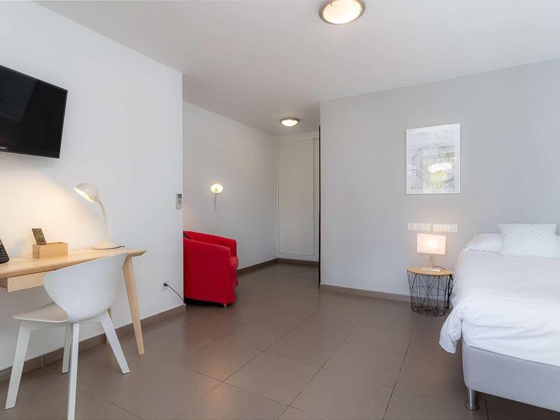 Minimalistisches Zimmer mit Bett, Schreibtisch, rotem Sofa und grauem Bodenfliesen.