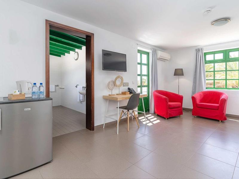 Helle, moderne Wohnküche mit roten Sesseln, großem Fenster, Schreibtisch und Mini-Kühlschrank.